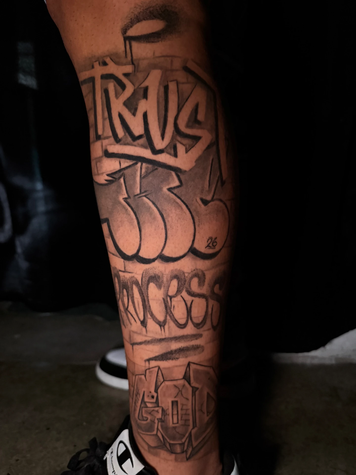 Tatuaje 'Trust The Process' en pantorrilla, lettering graffiti black and grey realizado por Santana Art